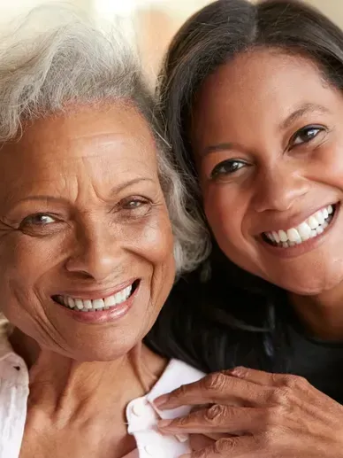 Two smiling Black women embracing; older woman with white hair, younger woman with dark hair.