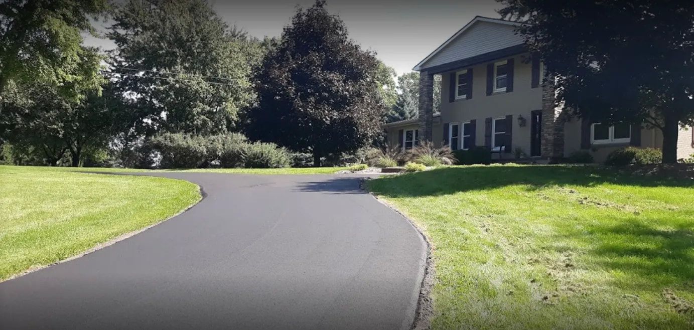 A driveway leading to a large house surrounded by trees and grass.