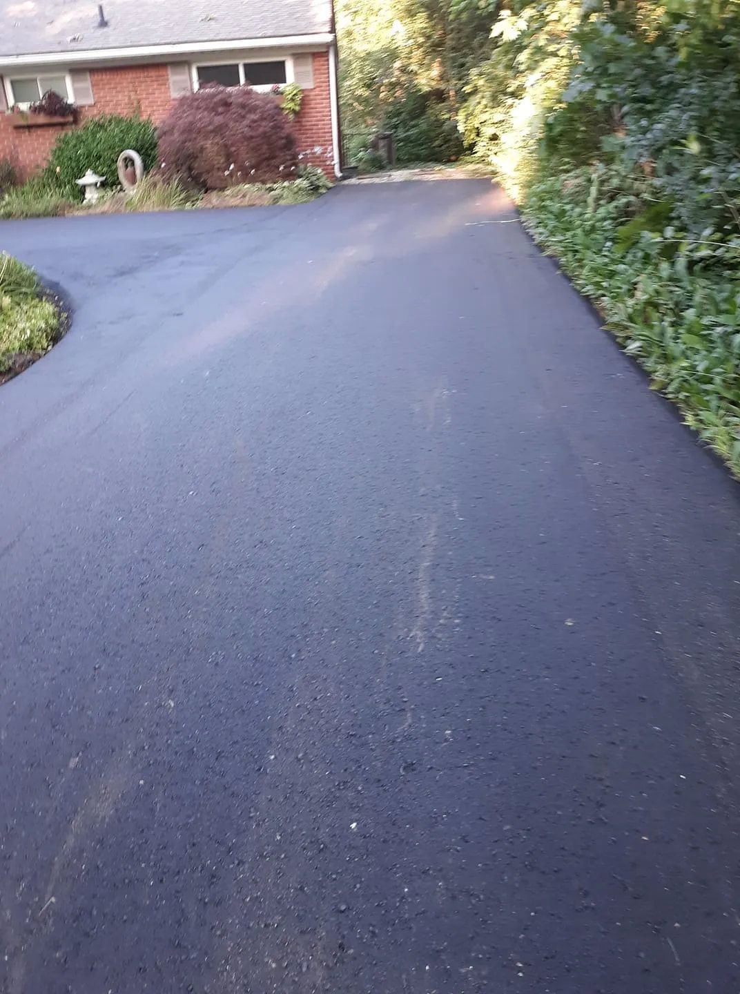 A black asphalt driveway leading to a brick house.