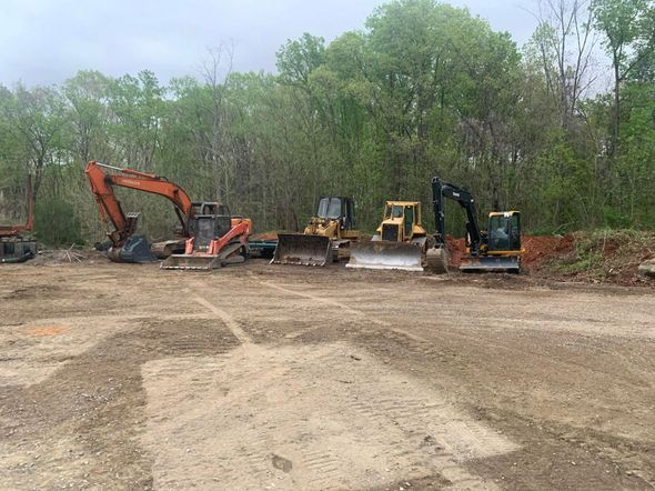 A group of construction vehicles are parked in a dirt field.