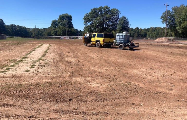 A yellow truck pulling a water trailer across a large, dirt field on a clear, sunny day.