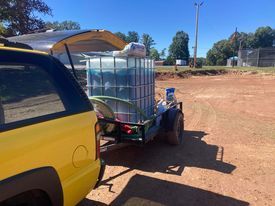 A yellow pickup truck with an open camper shell pulling a trailer with a large, full translucent water tank outside.
