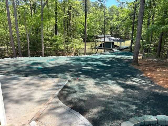 A sloped backyard freshly covered in green hydroseed, leading down toward a boat dock on a lake surrounded by trees.