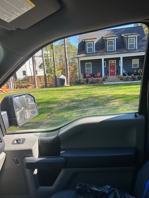 A dark blue two-story house with a red door and a front porch, seen through the window of a parked vehicle.