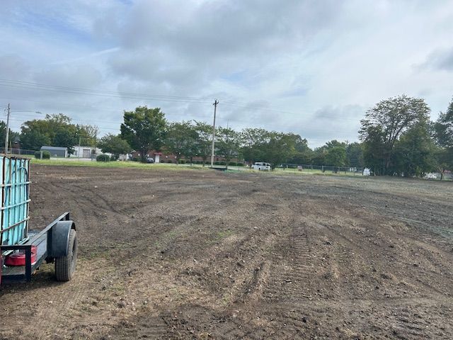 A freshly cleared, dirt-covered field on a cloudy day, with a trailer holding a large water tank in the foreground.
