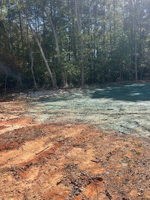 A construction site showing a patch of bare red dirt transitioning into an area covered with blue hydroseed mulch.