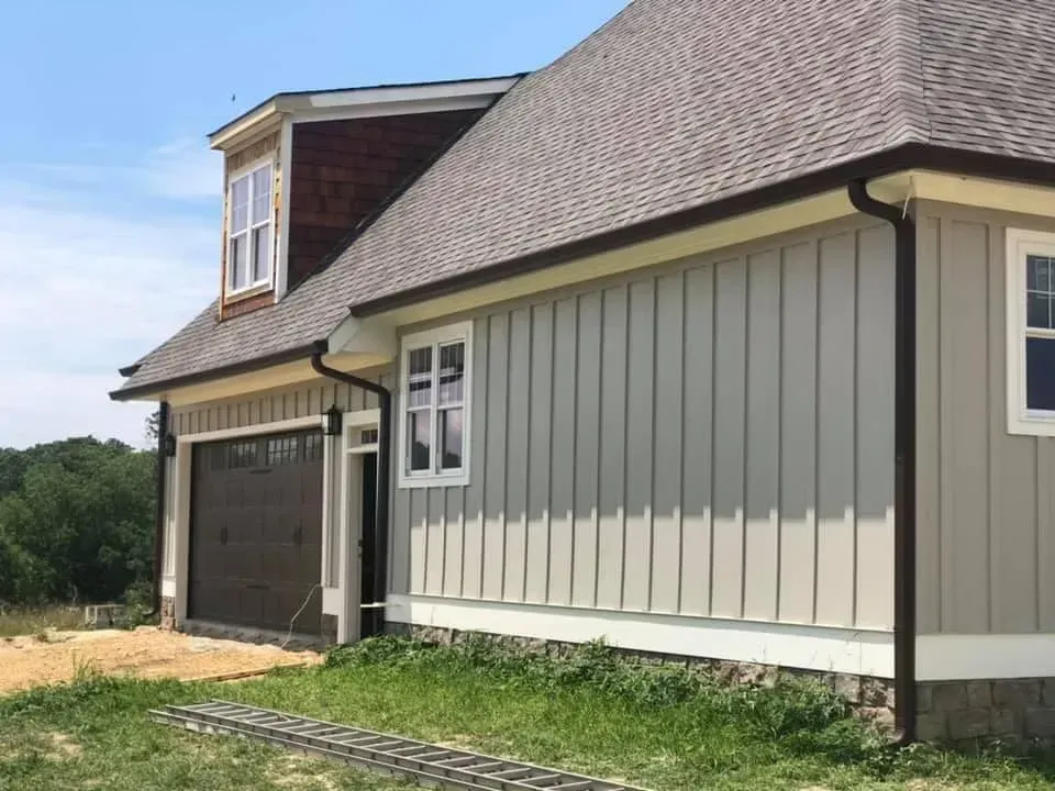 House exterior with gray vertical siding, brown roof and trim, garage door, and white-framed windows.