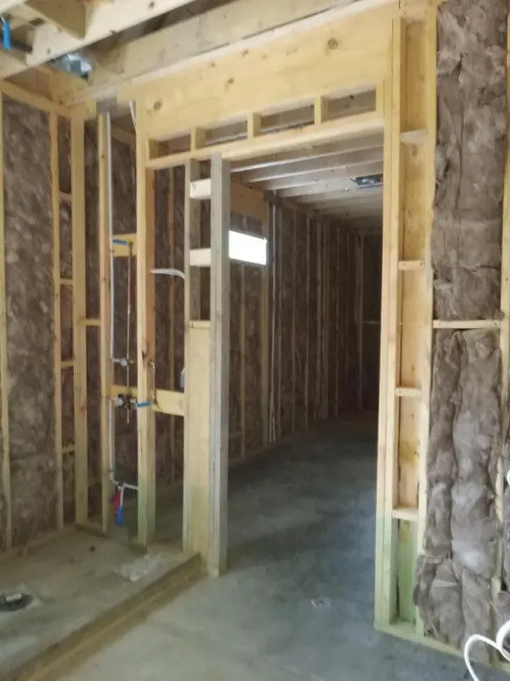 Interior of a room under construction, doorway, exposed wooden studs, insulation, unfinished concrete floor.
