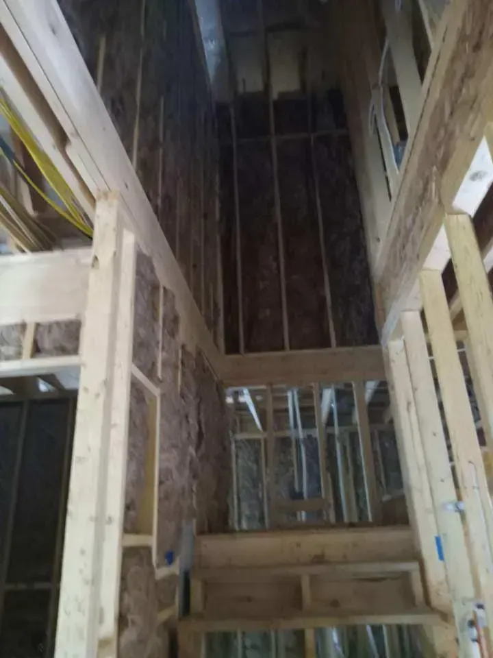Interior view of a building under construction, showing wooden framing, insulation, and electrical wiring.