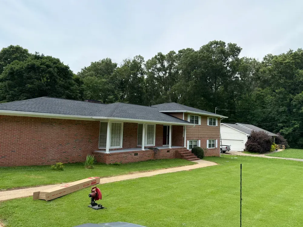 Red brick house with dark roof and green lawn, trees in background.