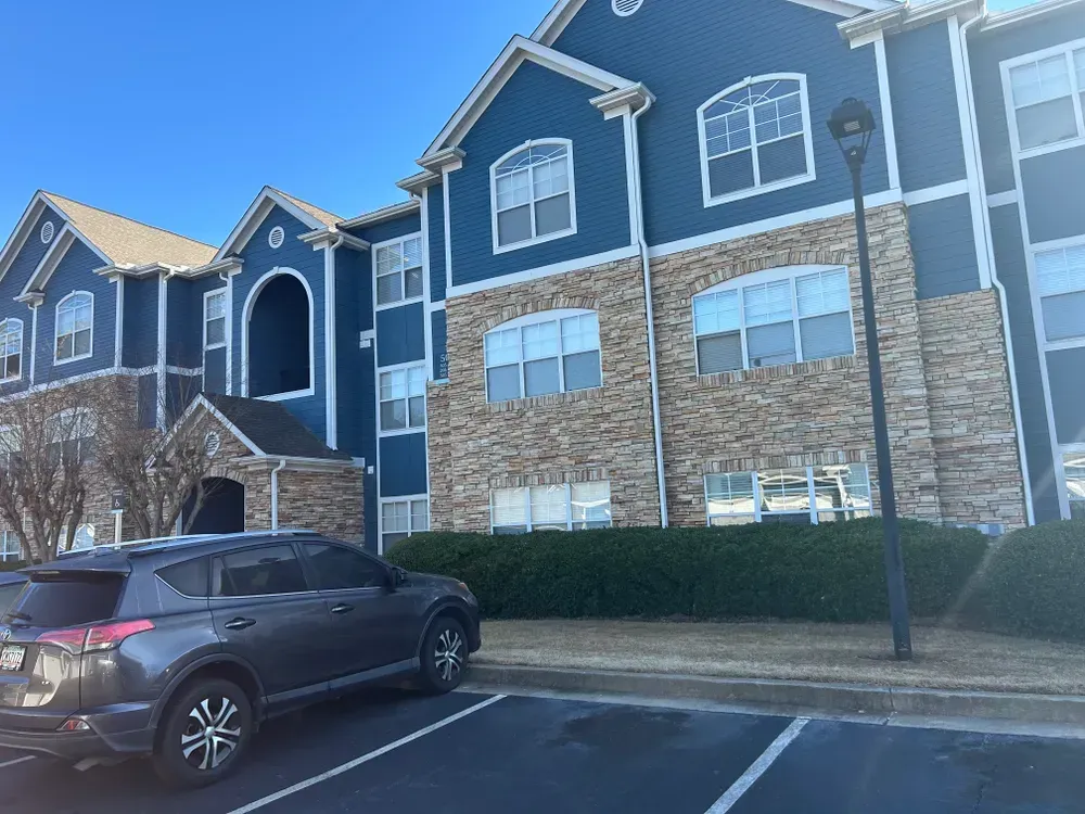 SUV parked in front of a multi-story apartment building with blue siding and stone accents on a sunny day.