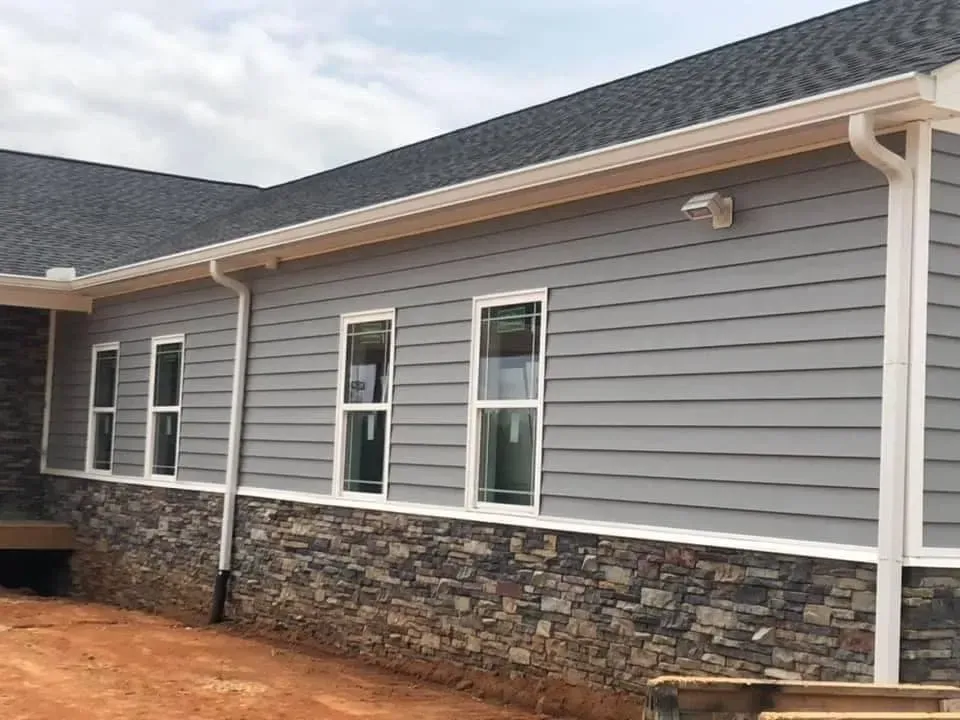 Gray siding house with stone base and white-framed windows, gutters, and roof.