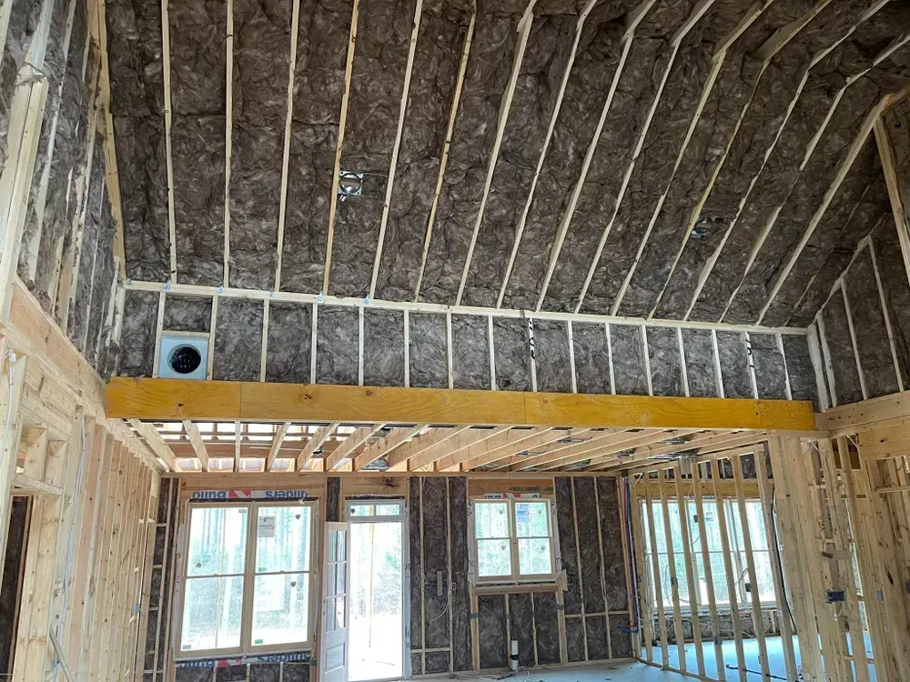 Interior framing of a house under construction with insulation in walls and ceiling.