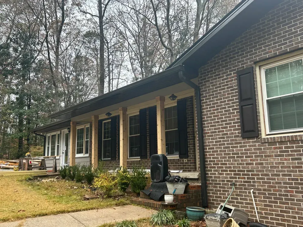 Brick house exterior with dark shutters, tan porch posts, and black gutters.