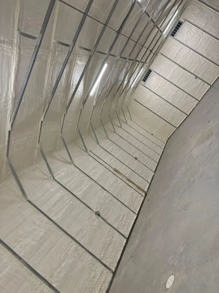 Interior view of a curved structure with metal supports and white insulation, possibly a building or vessel.