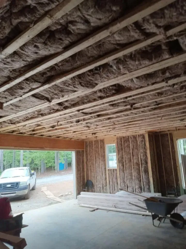 Interior view of a building under construction. Insulation installed between ceiling joists and wall studs.