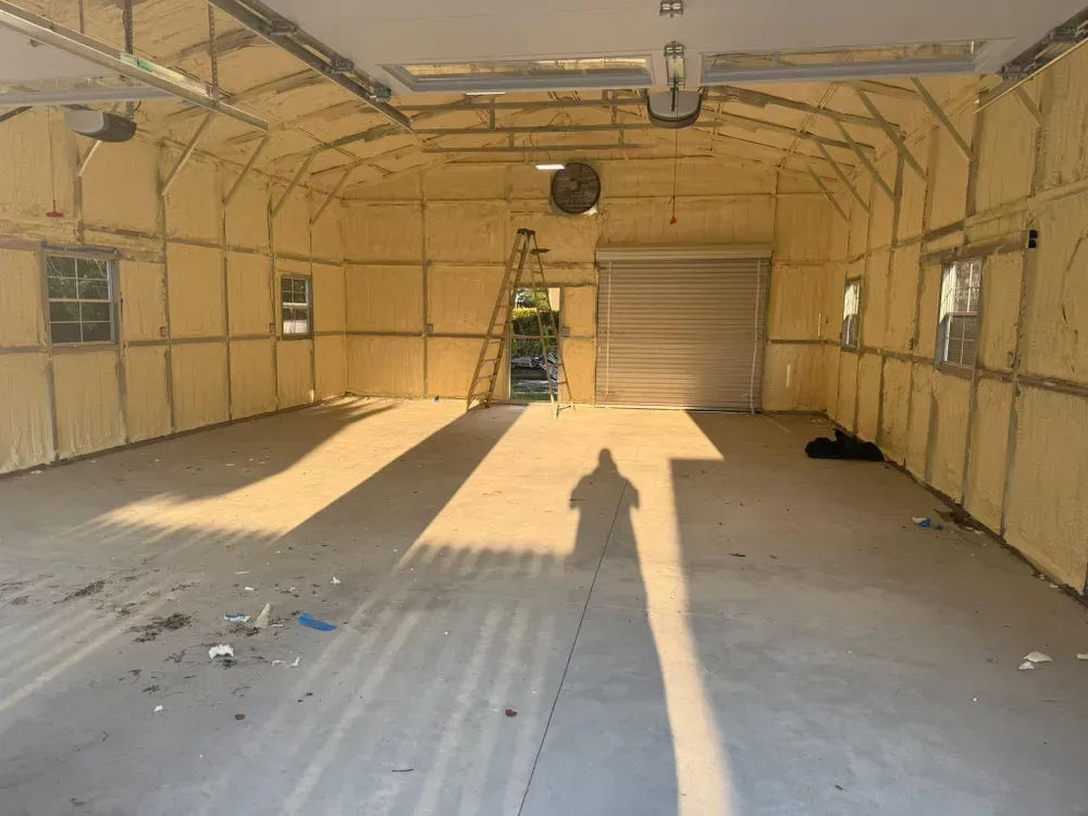 Interior of a garage with spray foam insulation. Sunlight casts shadows on the floor.