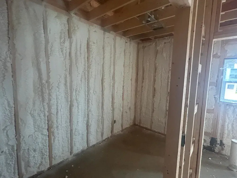 Interior of a room with spray foam insulation between wooden studs on walls and ceiling.