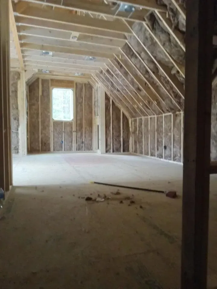 Interior of a room under construction, with wooden framing, insulation, and a window.