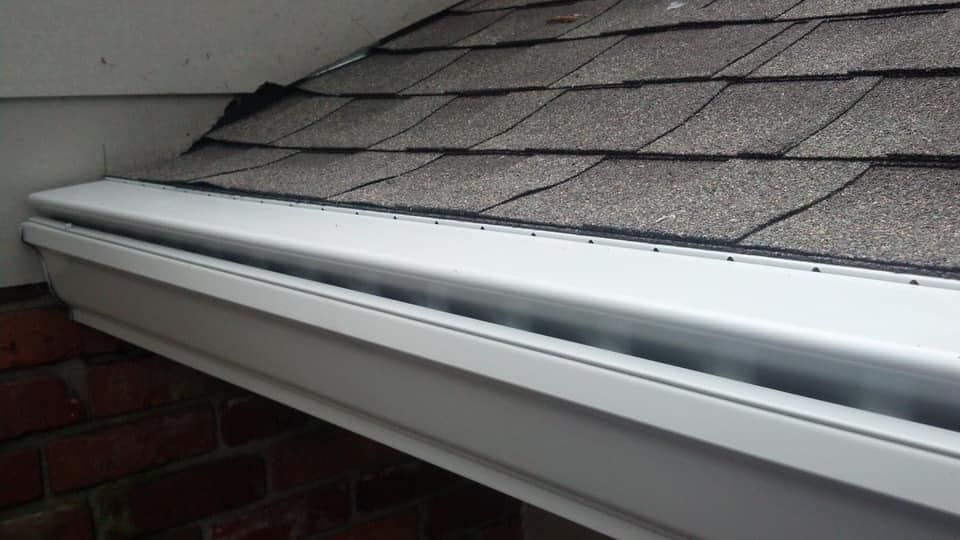 White gutter along the edge of a roof with dark brown shingles.