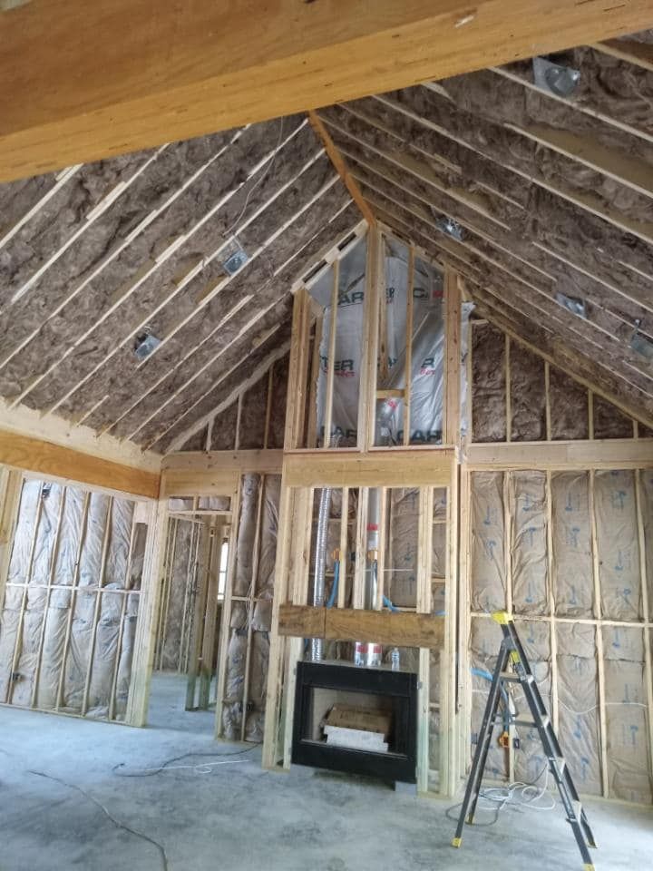 Interior of a house under construction. Studs and insulation are visible. A fireplace is framed in wood.