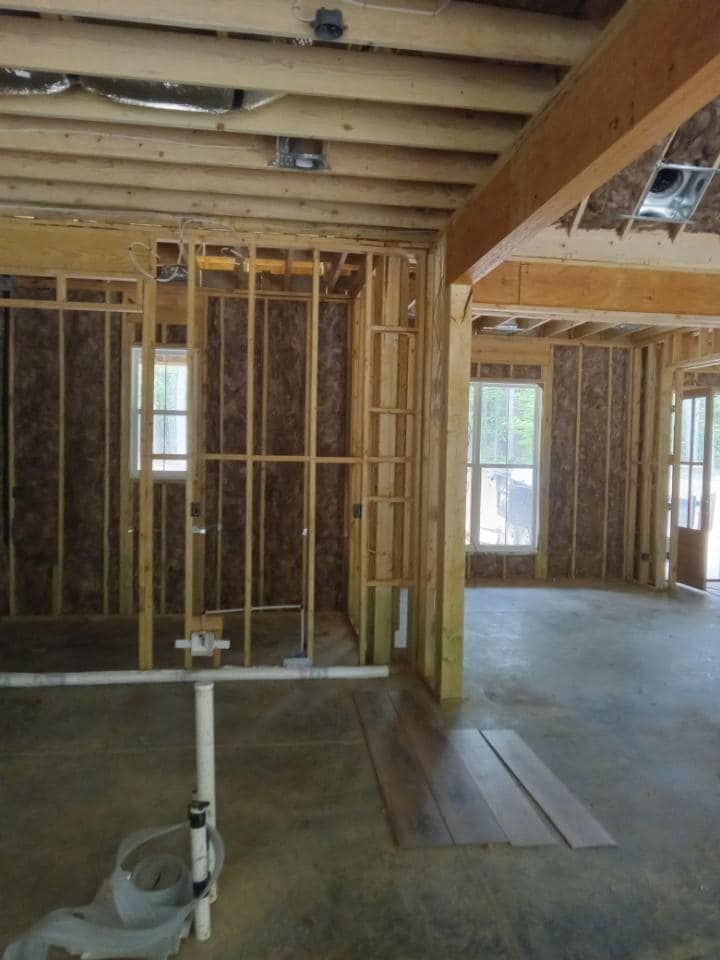 Interior of a house under construction; wooden framing, concrete floor, windows, and exposed insulation.