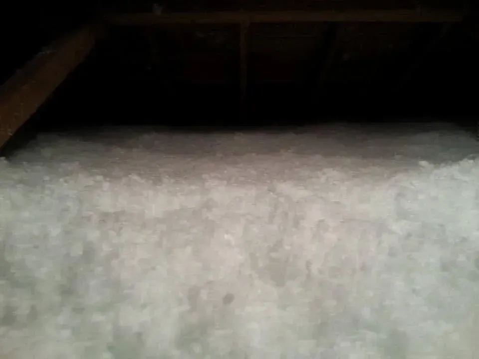 White insulation fills an attic space, viewed from below, against a dark background.