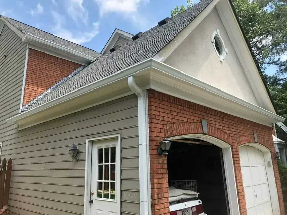Exterior of a two-story home with gray siding, brick, and a garage with an open door. White gutters line the roof.