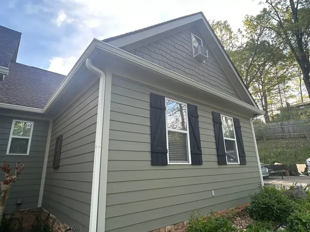 Green house exterior with black shutters, windows, and light blue sky.
