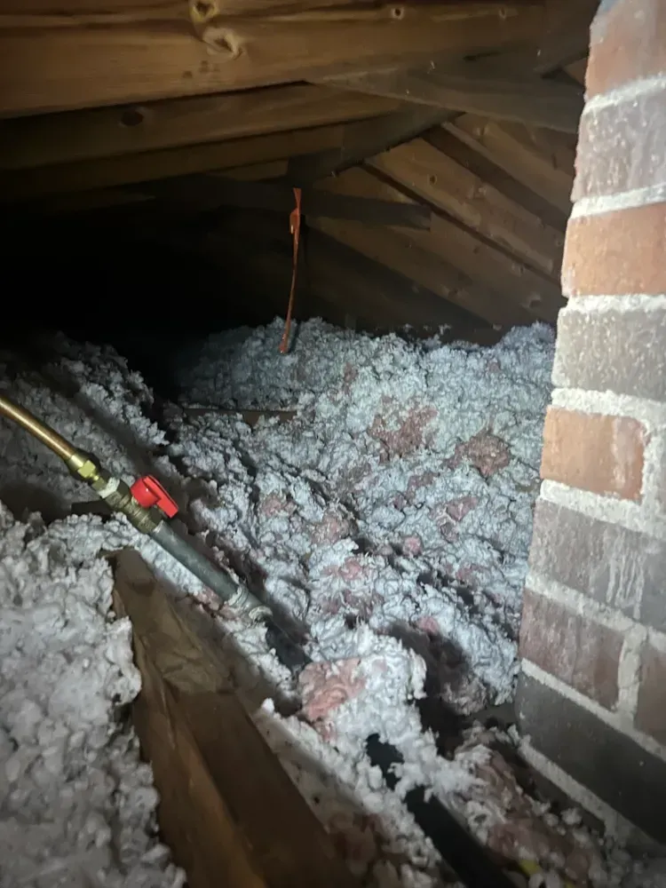 Attic interior with insulation, brick chimney, and pipes.