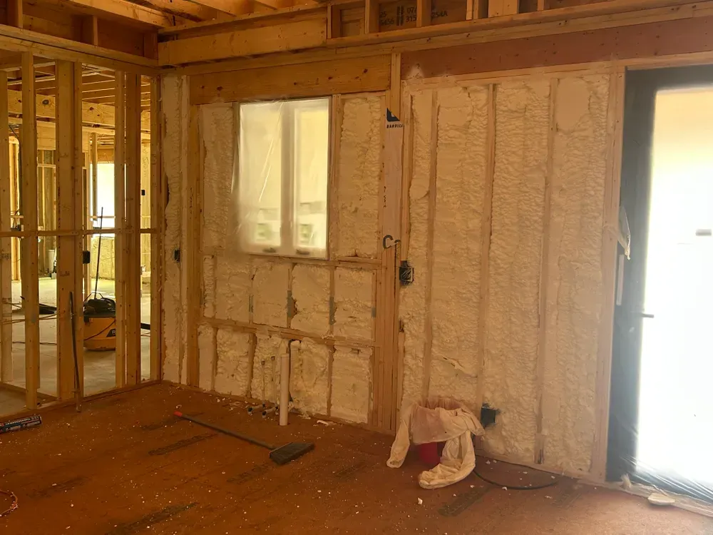 Interior of a room under construction, with spray foam insulation visible on the walls; unfinished wooden framework.