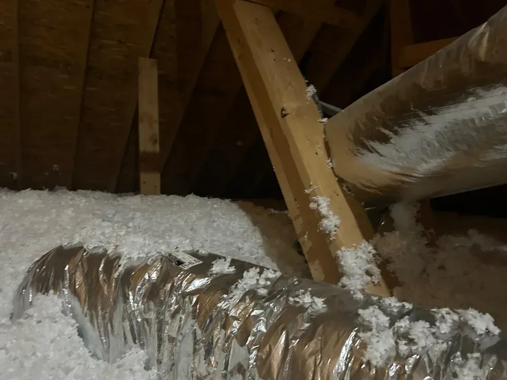 Attic interior with insulation, wooden beams, and ductwork.