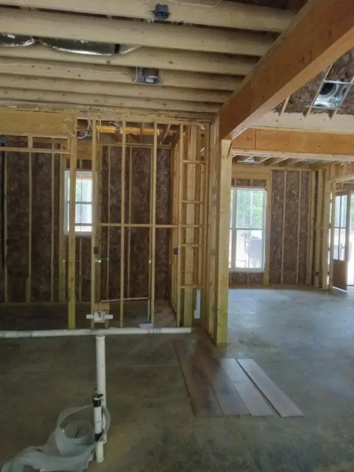 Interior view of a building under construction, showing wooden framing, insulation, and concrete floor.