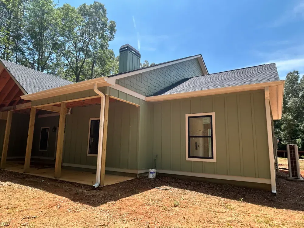 Green house with white trim, covered porch, and black-framed windows, against a blue sky.