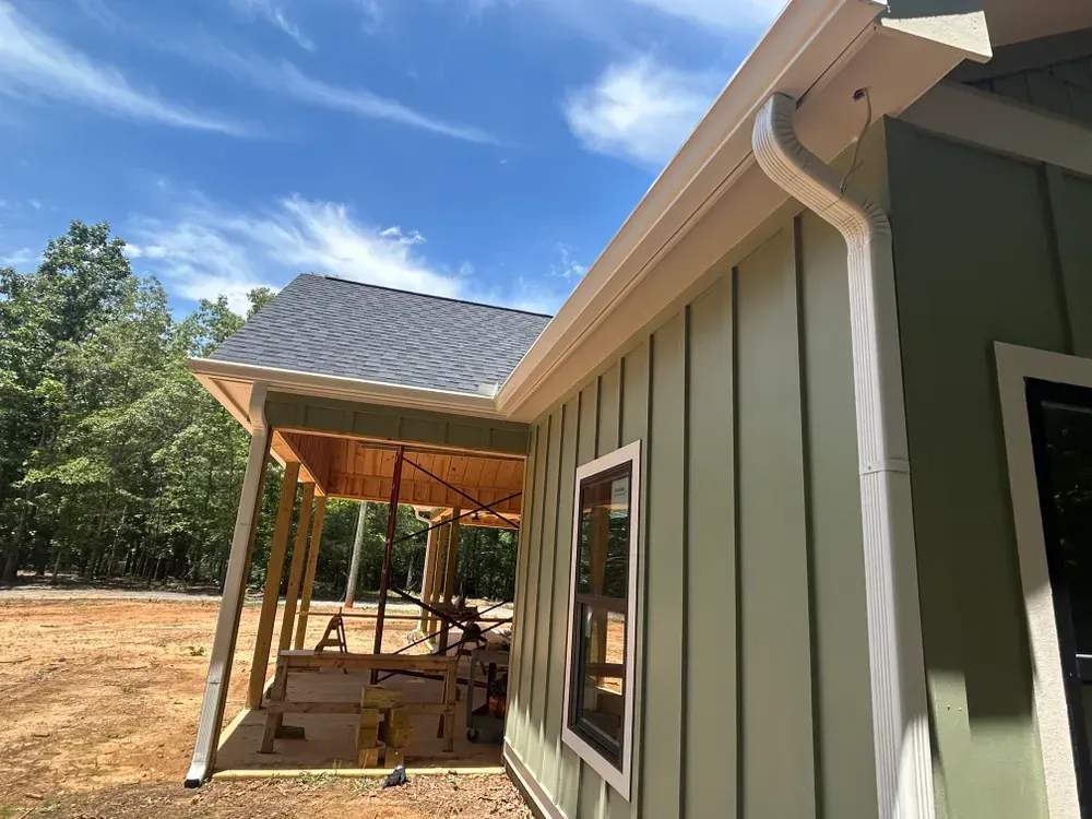 Green house exterior with white trim, gutters, and a covered porch under a blue sky.