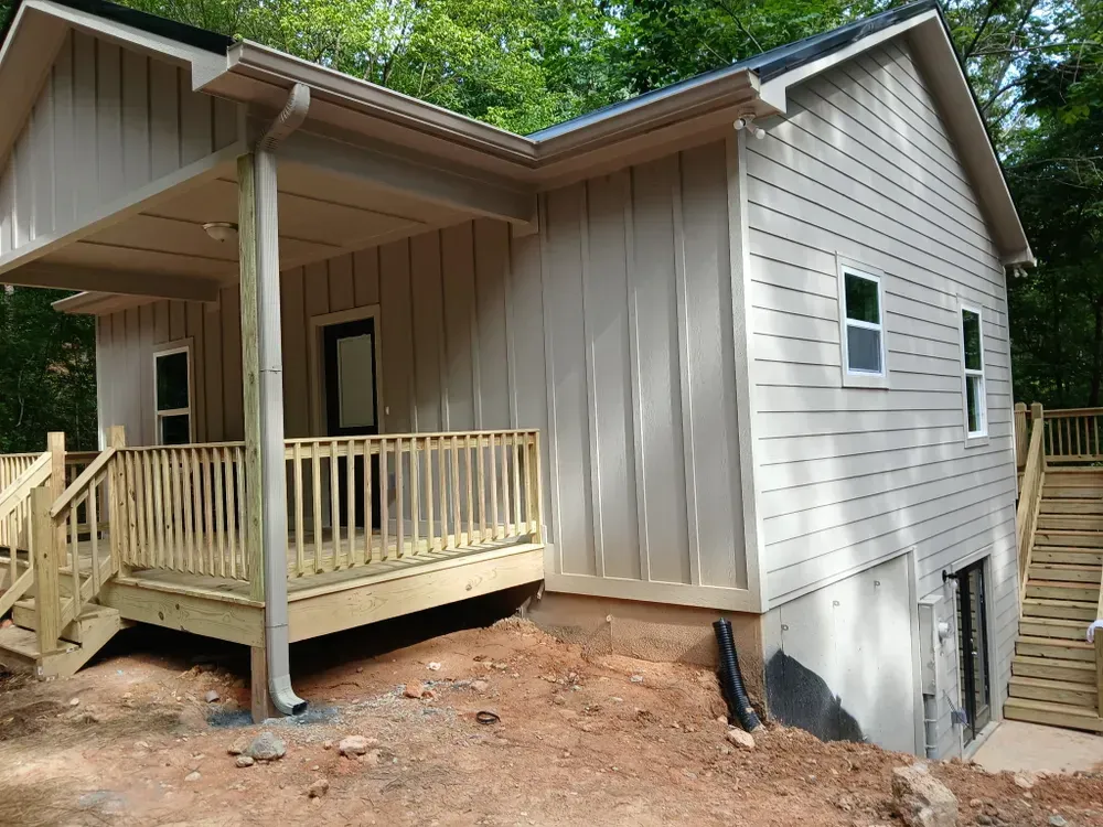Beige house with porch and stairs on a sloped yard.