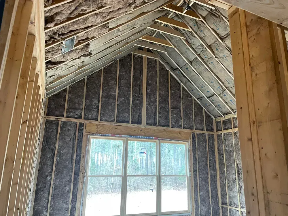 Interior view of a building under construction, showing wooden framing, insulation, and a window.