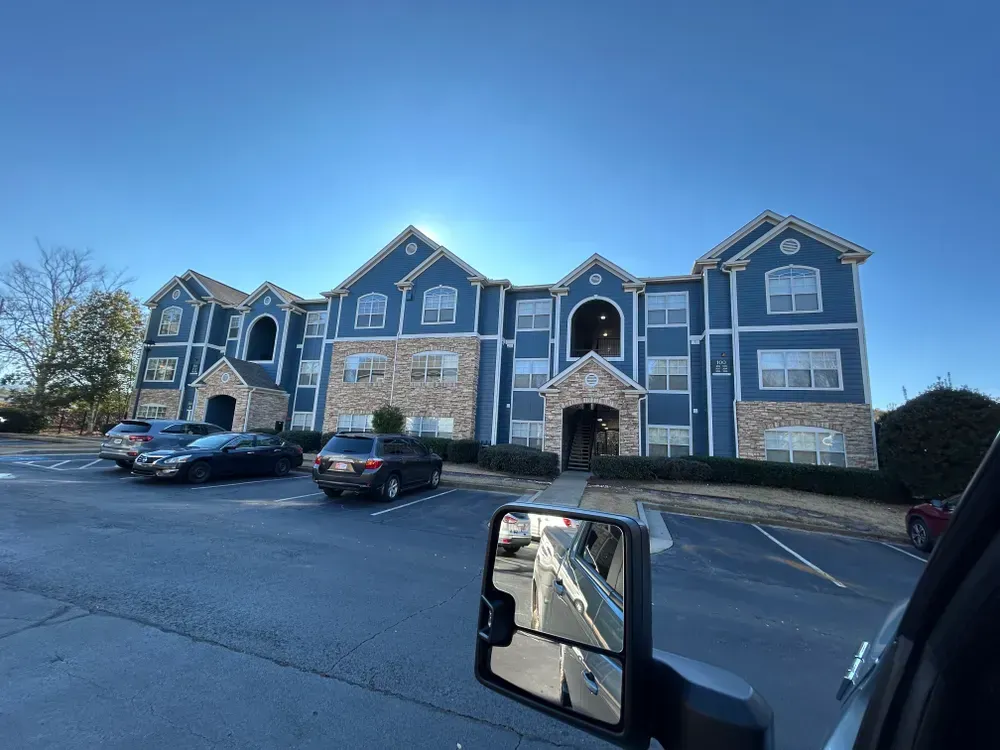 Blue apartment building with stone accents, parked cars, clear sky.