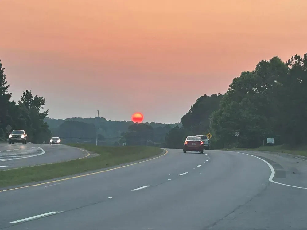 Sunset over a curving highway; cars driving on asphalt road, trees line the sides.