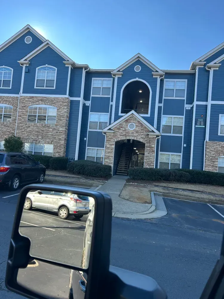Blue apartment building with stone accents; a car is reflected in the side mirror.