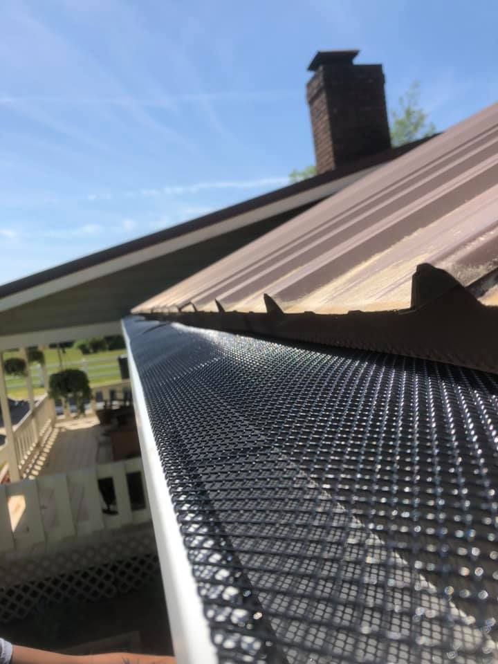 Black mesh gutter guard installed on a house roof. Blue sky and brick chimney in the background.