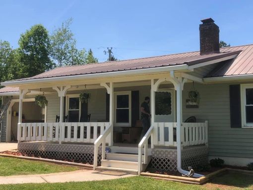 A house with a porch. Green siding, white railing, metal roof. Person standing in the doorway.