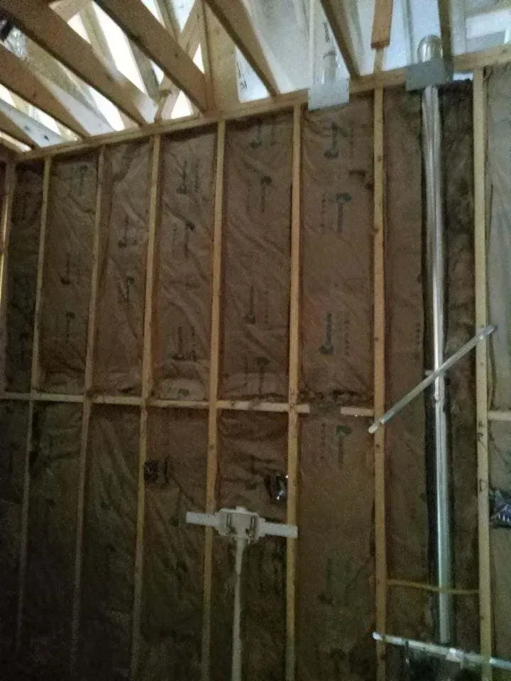 Interior wall under construction, wooden frame with insulation. Metal chimney pipe visible.
