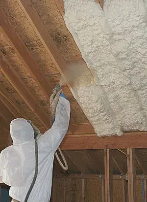 Person in protective suit spraying foam insulation in an attic.