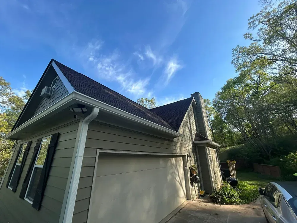 House with a dark roof and a light-colored garage door. The sky is blue with whispy clouds.
