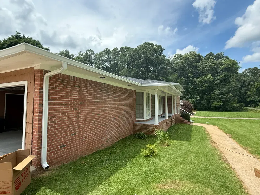 Red brick ranch-style house with white trim, gutters, and a garage. Green lawn with a path on a sunny day.