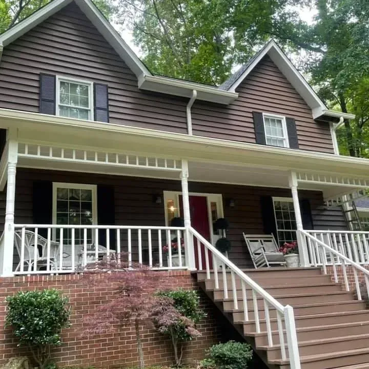 Brown house with white porch, brick base, and a red front door.