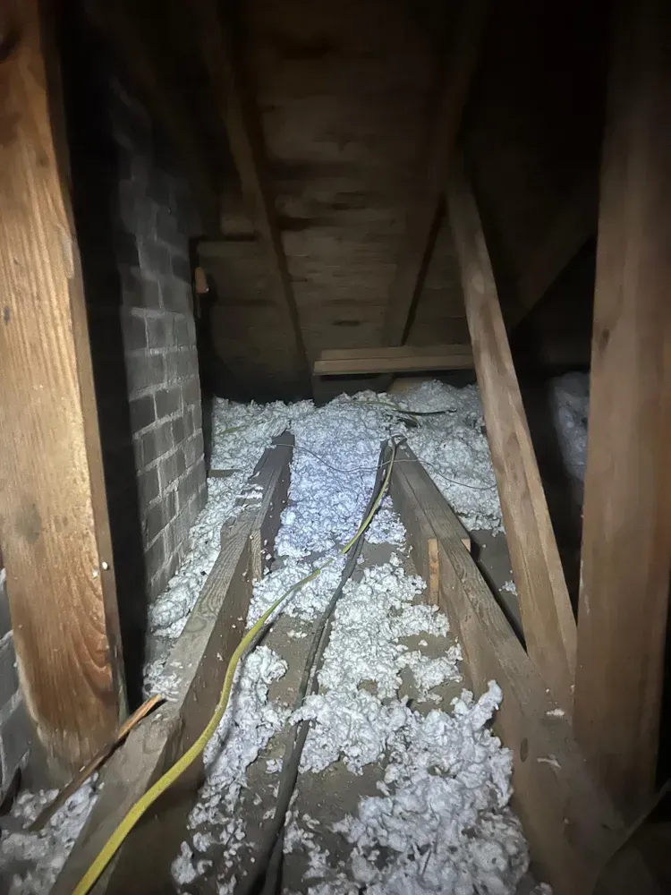 Attic space with white insulation between wooden beams and a brick wall.