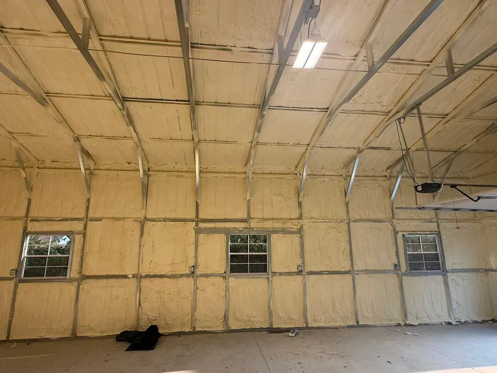 Interior view of a building with spray foam insulation on the walls and ceiling. Windows are visible.