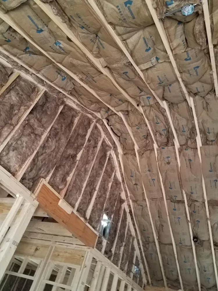 Interior view of a building under construction, showing insulation between wooden beams and framing.